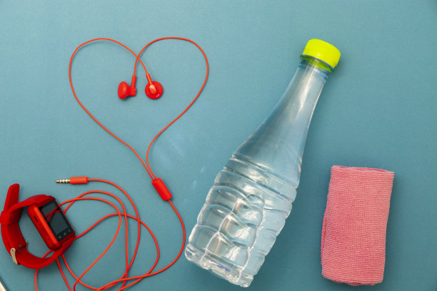 特写水瓶，手表和红色耳机，毛巾上的绿色背景，健身背景概念。图片下载
