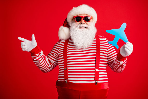 爷爷的照片灰胡子抱蓝色纸飞机直接手指空白穿圣诞老人圣诞服装吊带太阳镜条纹衬衫帽孤立的红色背景图片下载