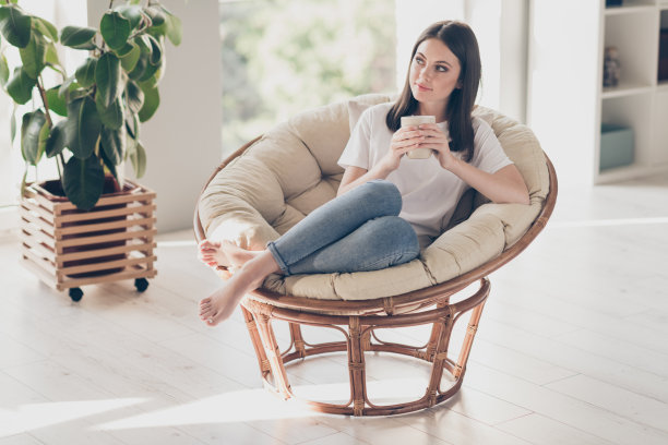 迷人的女孩全身照片，穿着休闲风格的衣服，坐在扶手椅，抱着咖啡杯梦想在房子公寓图片下载