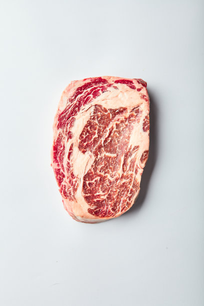 由大理石纹理的谷物喂养的牛肋眼牛排躺在白色的背景上。图片下载