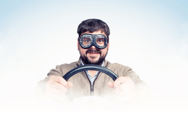 滑稽的大胡子男人戴着时髦的护目镜，方向盘，烟雾缭绕，浅蓝色背景。前视图。车司机的概念图片下载