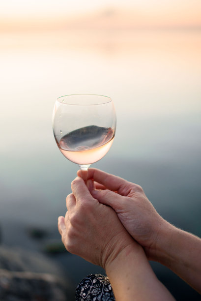 一个年轻女孩手里拿着一只漂亮的杯子，上面有粉红色的葡萄酒。日出时喝一杯酒。浪漫的早餐图片下载