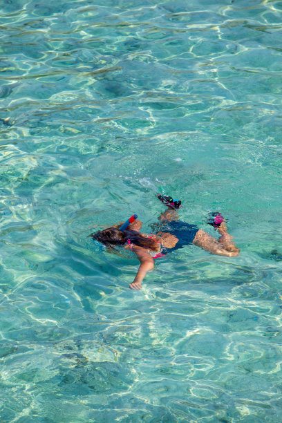 一个戴着潜水面罩的女孩趴在清澈的水中游泳。从上往下看。图片下载