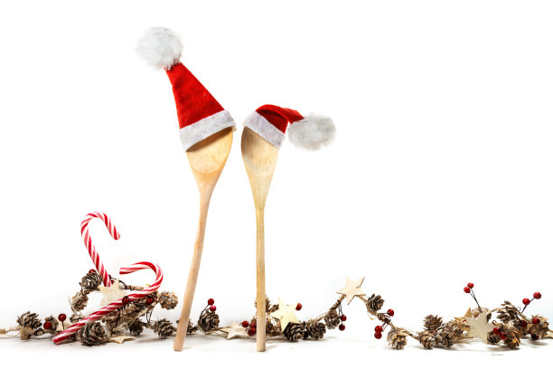 两个木制烹饪勺子，红色的圣诞老人帽子和圣诞装饰花环，糖果手杖，锥形，星星和人造浆果，孤立在一个白色的背景，复制空间图片下载