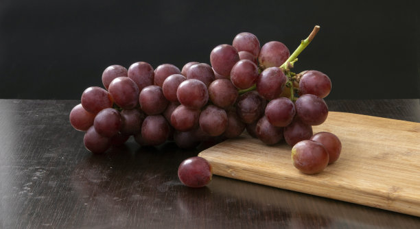 水果和葡萄的静物画和切菜板在黑色的背景上图片下载