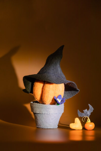 在深橘色的背景下，用黑色的蝙蝠做的锅里的南瓜毛毡。的心。创意艺术万圣节派对。图片下载