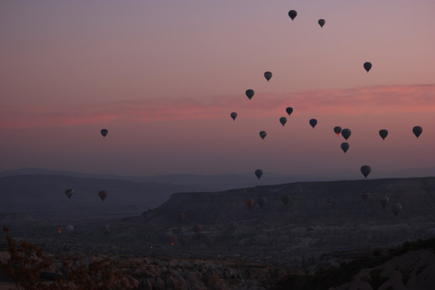 在日落的天空中，热气球飞过岩石景观。图片下载