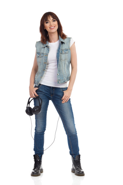 快乐的年轻女子站着，拿着耳机，看着镜头图片下载