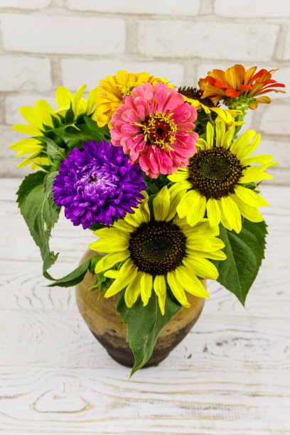 白色砖墙边，古色古香的陶罐上放着一束鲜花图片下载