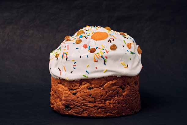 撒有糖霜的圣诞蛋糕，装饰有干杏，葡萄干和彩色装饰。潘妮托内被孤立在黑暗的背景上。图片下载