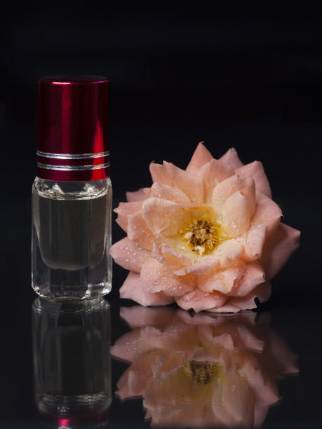 浓缩香水在一个小瓶子与粉红色的花茶玫瑰在黑色的背景图片下载