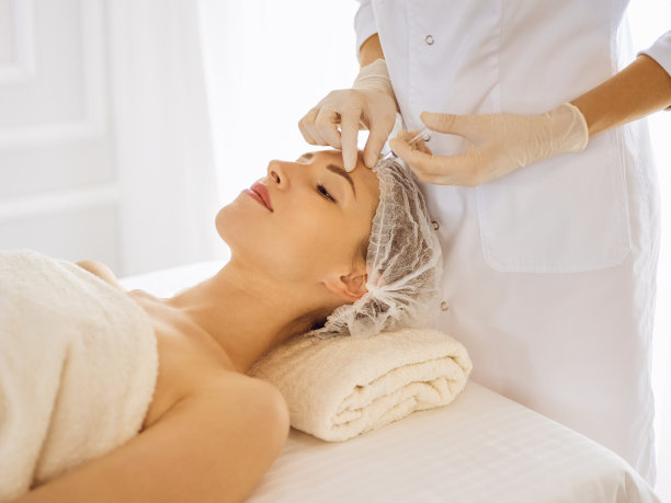 闭着眼睛接受美容注射的美女。美容师医生用注射器给女性脸部做美容手术图片下载