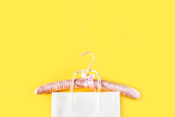 空的粉红色衣架和黄色背景的白色纸袋。销售和购物概念。图片下载