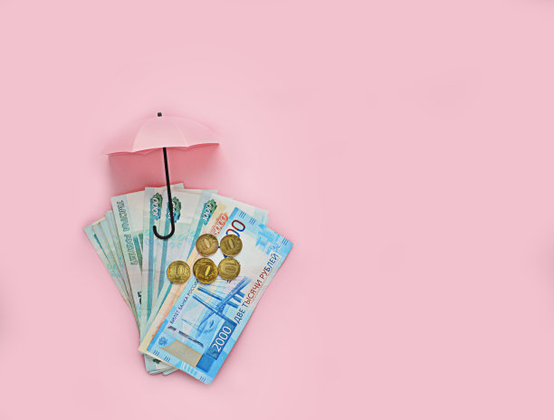 面值为1、2000俄罗斯卢布的纸币和粉红色背景上的一堆硬币，以及打开的粉红色雨伞。储蓄、收入、业务、银行、贷款、存款的概念。保护存款和金钱。平的。处理空间。图片下载