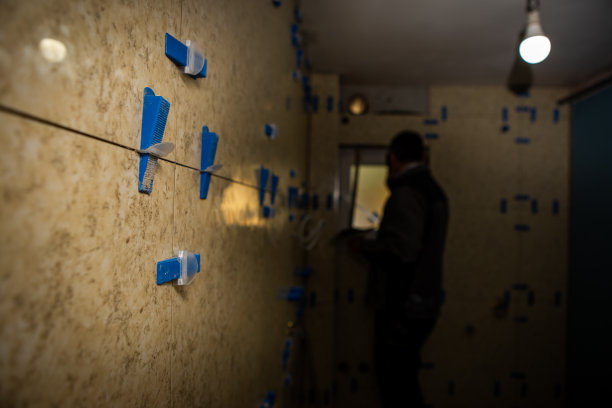 浴室的装修正在进行中。工人把大瓷砖贴在墙上。图片下载