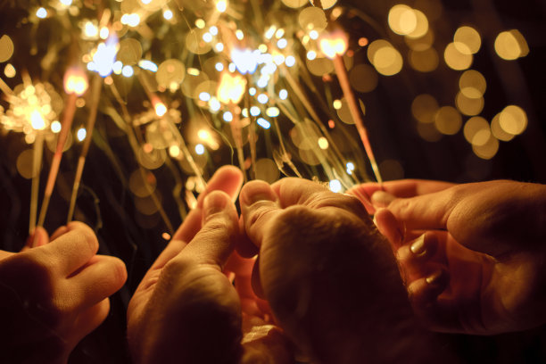 在圣诞彩灯的背景上，镜头拉近了三个人的手，手里拿着烟花图片下载