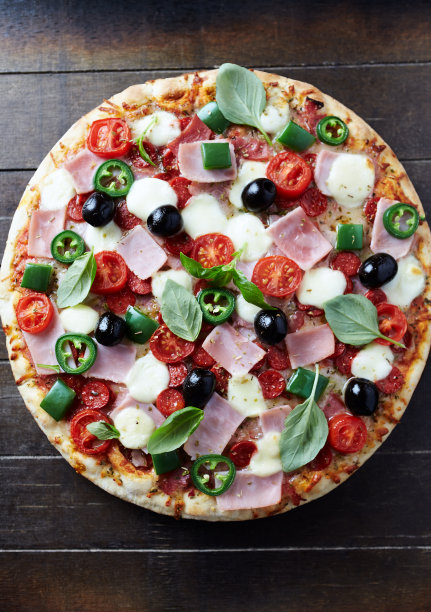 火腿、马苏里拉芝士、樱桃番茄、青椒、墨西哥胡椒、黑橄榄和新鲜罗勒。深色木制背景。前视图。图片下载