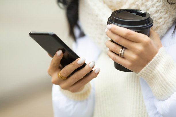 女性的手拿着智能手机和一杯咖啡在户外素材图片