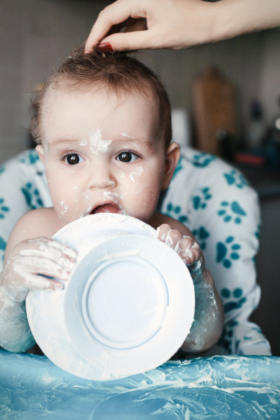 脏兮兮的小男孩坐在高脚椅上，玩着从酸奶里拿出来的脏盘子。图片下载