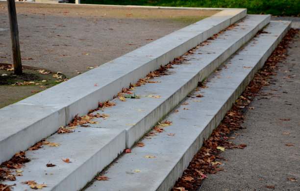 通往公园的混凝土楼梯同时也可以用作长椅。灰水泥干净光滑，水泥表面光亮。花岗岩方砖铺装和打粒砾石路。长满植物。防打滑边缘图片下载