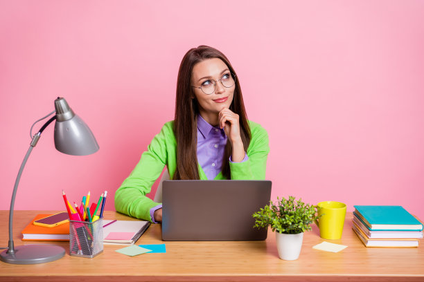 体贴的女孩坐桌子工作笔记本电脑触摸手下巴看copyspace认为孤立的柔和的颜色背景图片下载