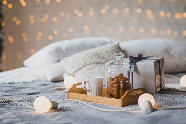 在装饰好的房间的床上放着一杯热茶和圣诞饼干，背景是节日的灯光。图片下载