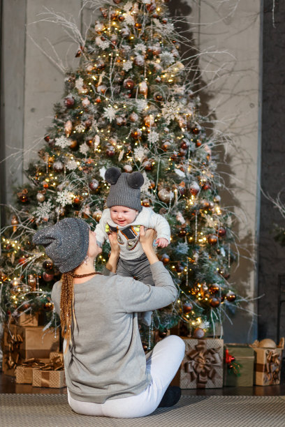 妈妈和女儿在圣诞树旁玩耍。为圣诞节拍摄照片。人们戴着编织的帽子。灰色的衣服图片下载