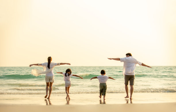 幸福的亚洲家庭父母和两个孩子的男孩和女孩手牵手一起走在海滩上在夏天的日落。父亲，母亲和孩子享受和有乐趣的户外假期假期。图片下载