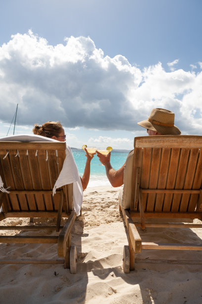 一对夫妇在热带海滩的柚木躺椅上喝着鸡尾酒敬酒图片下载