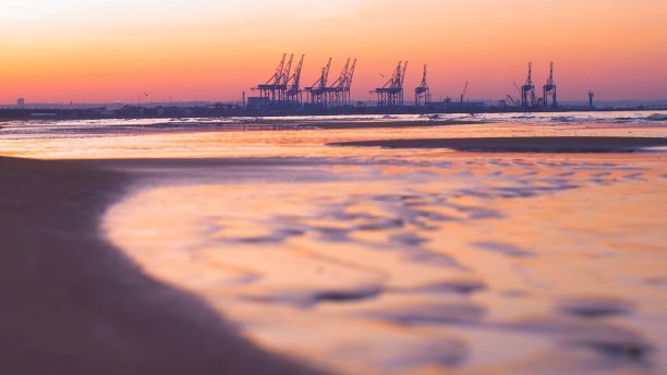 日落时分，波罗的海沙滩上的集装箱码头起重机为背景图片下载