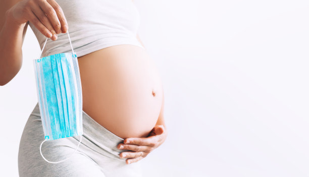 特写孕妇的肚子和医用口罩。大流行期间的保护和预防、孕妇及其婴儿健康的概念。图片下载
