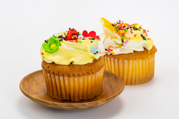 香草纸杯蛋糕配以香草奶油糖霜，并在白色背景的木盘上撒上五颜六色的糖屑。图片下载