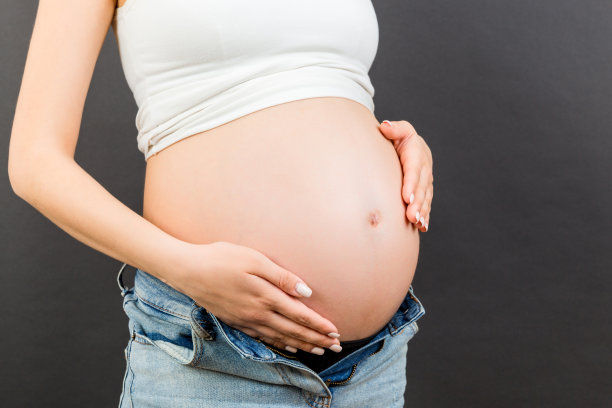 裁剪的图像孕妇在无拉链的牛仔裤显示她的宝宝在彩色的背景与复制空间。等待一个婴儿的概念图片下载