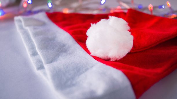 圣诞老人的红帽子和白色棉球躺在一个花环的背景上。圣诞和新年。超额支付的属性。文本。副本的空间。有选择性的重点。图片下载