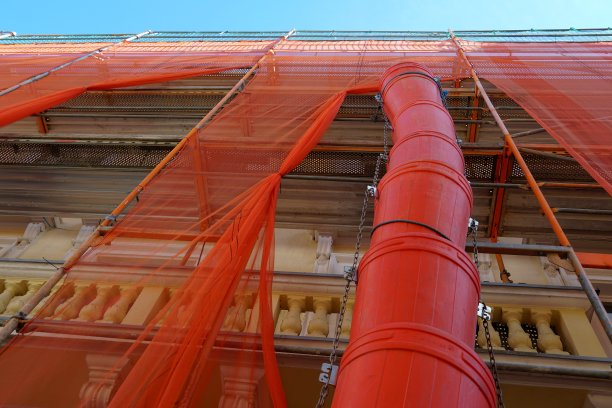 为清除垃圾而重建的历史建筑外立面上的红色垃圾槽或碎片槽。房子盖着红色的防护网。这张照片是低角度拍摄的。图片下载