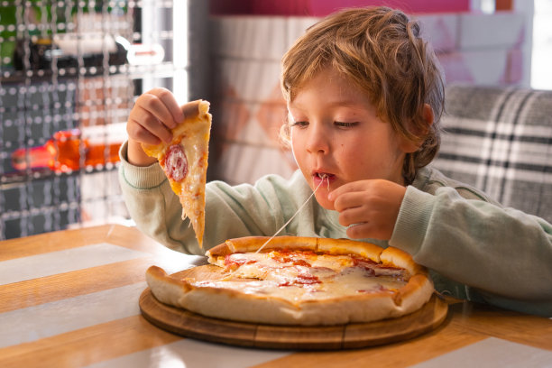 可爱的男孩在快餐店吃披萨。图片下载