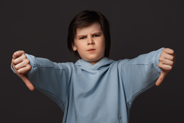 小白脸的肖像，拇指朝下。不像，不喜欢，失败手势的概念。工作室拍摄，灰色背景图片下载