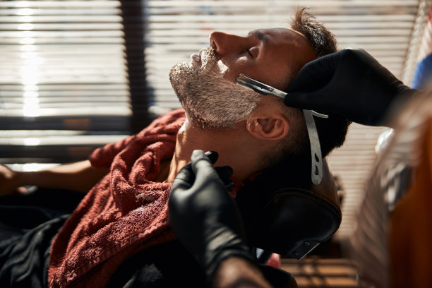 男理发师用老式直剃须刀刮男人的胡子图片下载