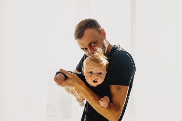年轻的父亲和他可爱的孩子。在阳光明媚的房间里扮演超人图片下载