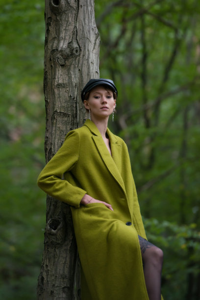 穿着绿色外套的时尚年轻女子在森林里摆姿势图片下载