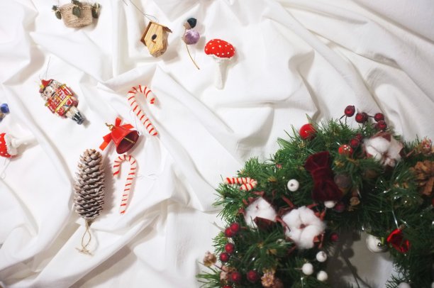 圣诞或新年花环用冬青浆果，棉花花，松果，其他传统装饰红色，白色和绿色。圣诞节日庆祝装饰在白色皱巴巴的床单背景图片下载