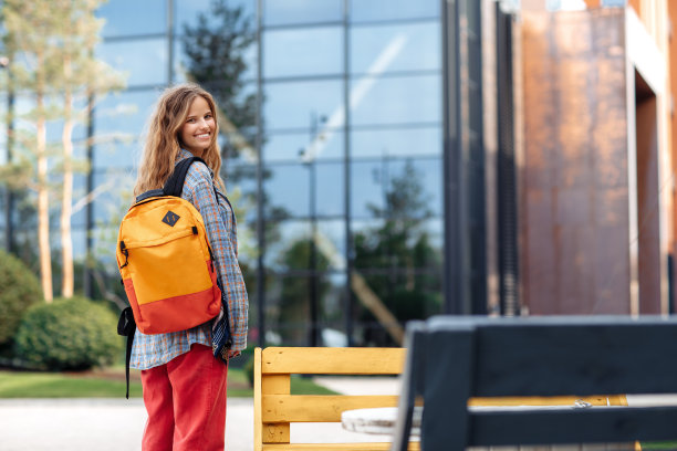 开朗年轻的金发时髦女学生背包回头看相机。图片下载