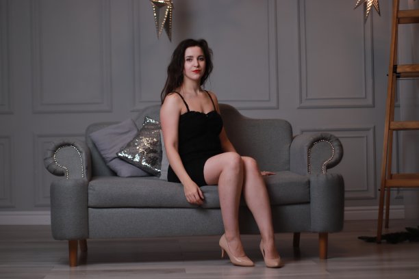 性感迷人的黑发在黑色紧身连衣裙在灰色的沙发在一个装饰大星星的灰色房间。工作室拍摄图片下载