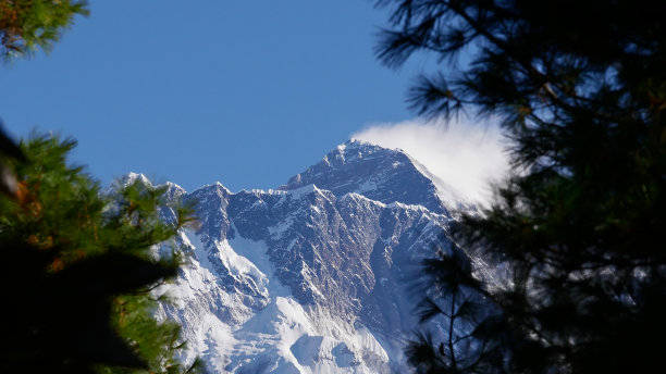 第一次看到伟大的珠穆朗玛峰的顶峰(顶峰:8848米)在珠穆朗玛峰基地营地徒步通过树木之间的一个差距，在喜马拉雅山，尼泊尔的Namche Bazar。图片下载