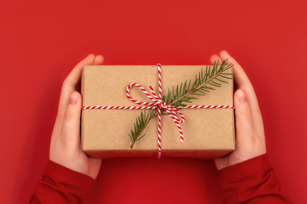 女孩手握圣诞礼物。红底牛皮纸包装礼品。图片下载