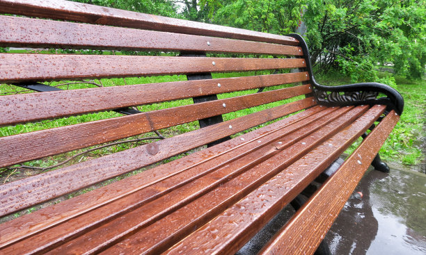 公园里下着大雨。雨滴落在木凳上。图片下载