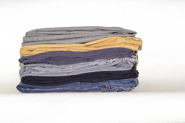 不同颜色的牛仔裤摞在白色的表面上。它们是黑色，棕色，蓝色和黄色图片下载