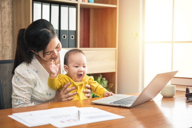 快乐的母亲在网上工作，用笔记本电脑抱着她的小儿子在家办公图片下载