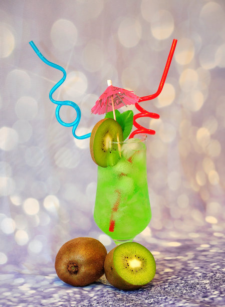 高脚杯的绿色饮料，以猕猴桃汁为基础，以冰和吸管为装饰，灰色闪亮的背景上有一把雨伞。图片下载