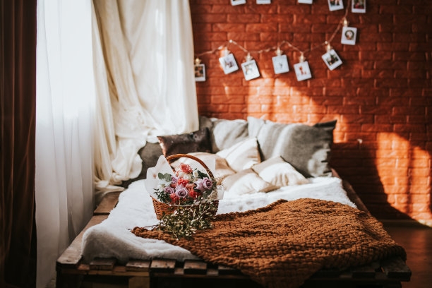 一张大床的托盘和枕头，在床上有一个大篮子的不同类型的花，一个花环的照片在砖墙上，阳光透过窗户选择焦点图片下载
